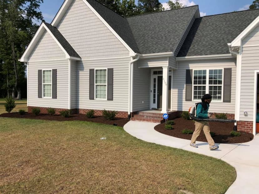 Person walking past a modern gray house with a well-maintained yard and shrubs.